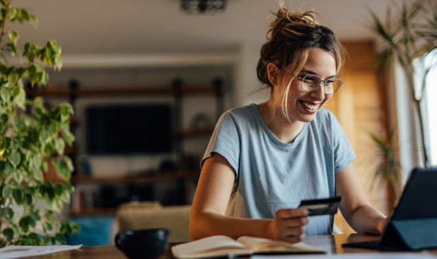 A woman smiles while looking at the computer and holding a debit card in her hand