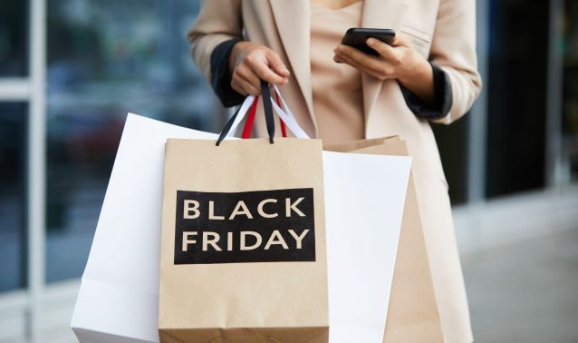 A woman holding bags looking at her phone during Black Friday shopping.
