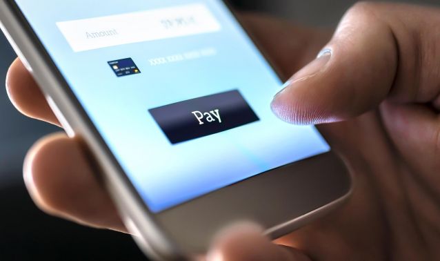 A thumb clicks on the payment prompt screen on a cell phone.