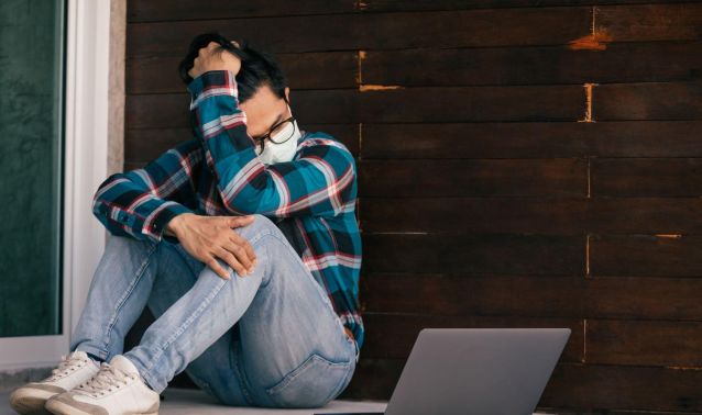 A young man wearing a mask looks at his laptop.