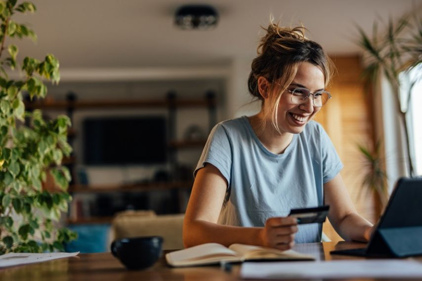 A woman smiles while looking at the computer and holding a debit card in her hand