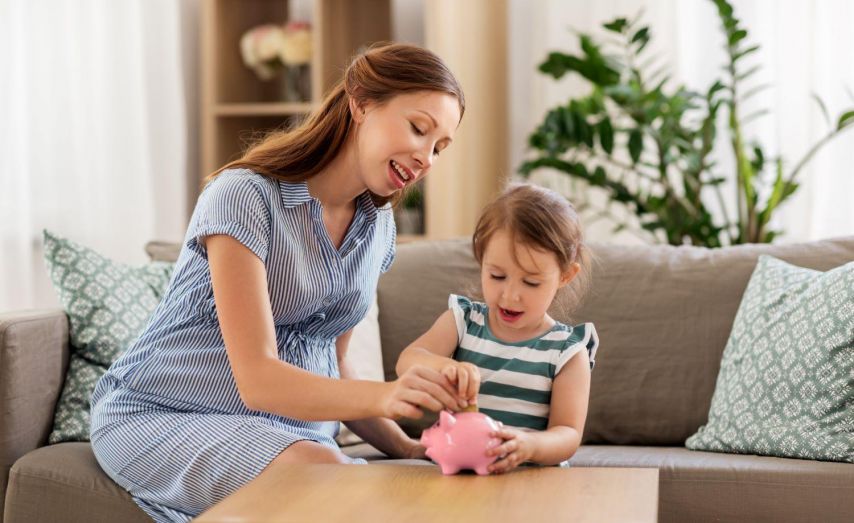 A mom helps her daughter put money in a piggy bank.