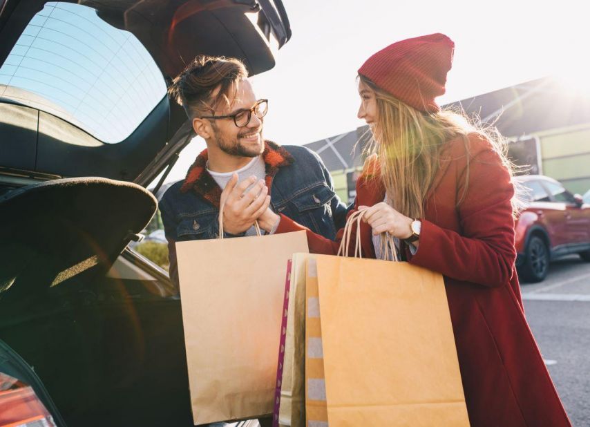 Couple putting shopping bags into trunk of car while smiling